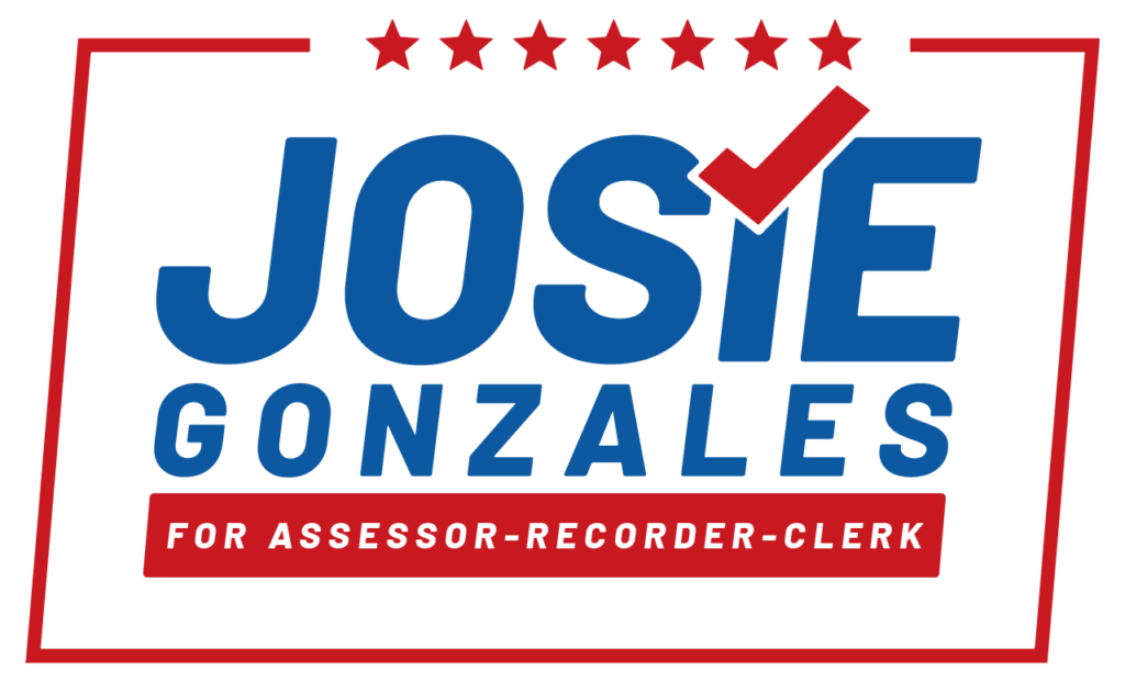 A campaign logo with blue text reading "Josie Gonzales" and "For Assessor-Recorder-Clerk" in red. A red checkmark replaces the dot over the "I" in "Josie." Six red stars line the top of the logo, all within a red rectangular border.